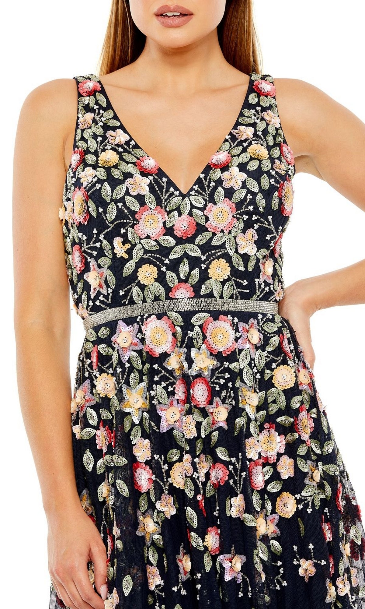 A woman wears the Mac Duggal 5527 Floral-Embroidered Party Dress—a sleeveless, tea-length black dress with colorful floral embroidery and a V-neckline—her right hand on her hip, highlighting its semi-formal elegance.